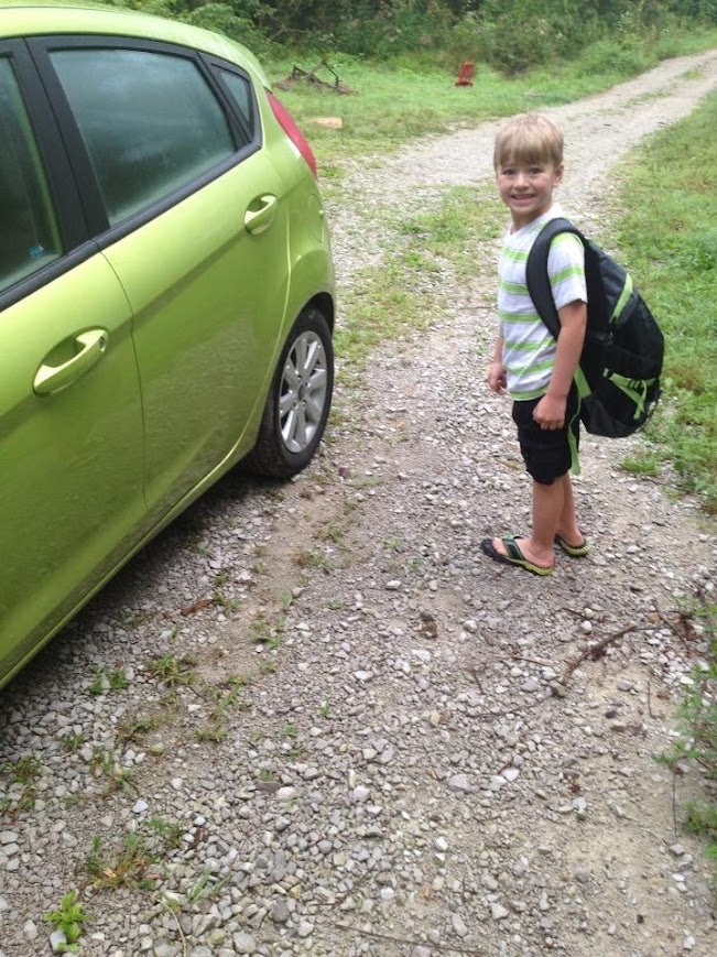 A little boy with a backpack on stands next to a bright green Ford Fiesta